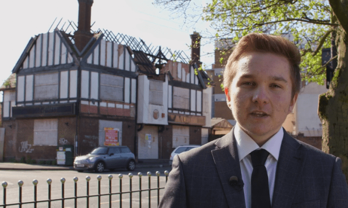 Elliott a student stands by the Bulls Head Pub 2016. The roof is caved inn and the pub boarded up.