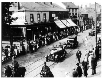 B+W photo of George Inn Public House and High Street 1900s showing a procession of cars led by two horse mounted police officers people line the route